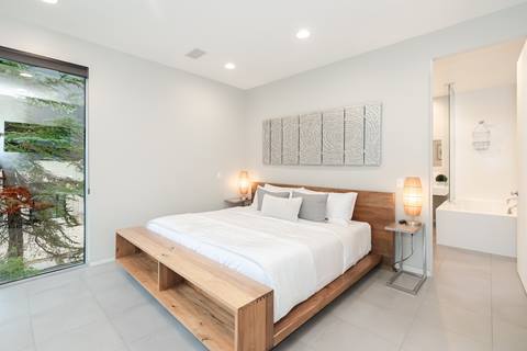 Bright bedroom with king bed, wood frame, white bedding, modern lamps, and ensuite bathroom.