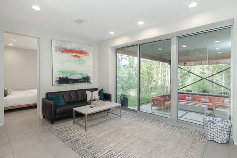 Living room with black leather sofa, coffee table, large abstract painting, and sliding glass doors opening to outdoor seating area.