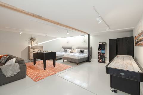 Game and guest room with foosball table, shuffleboard, arcade game, two beds, and bright orange rug.