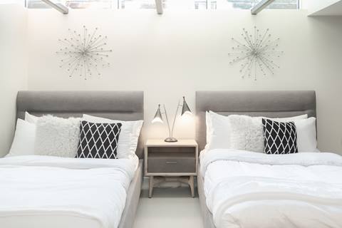 Double bedroom with two beds, gray upholstered headboards, geometric pillows, and modern lamps.