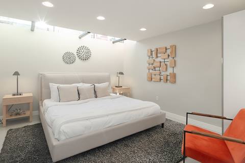 Bedroom with king bed, white bedding, neutral décor, orange accent chair, and modern wall art.