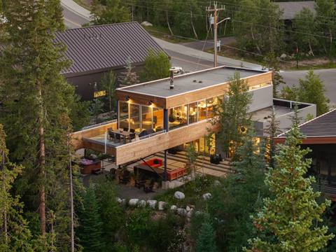 Zoomed out viw of nestled modern mountain lodge with surrounding  trees. 