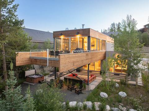 Modern mountain lodge with luxurious wooden exterior and deck with red furniture. 