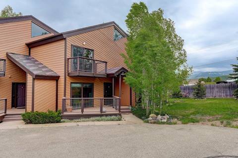 Exterior of mountain lodge with leafy aspen in the front lawn and the driveway in the foreground. 