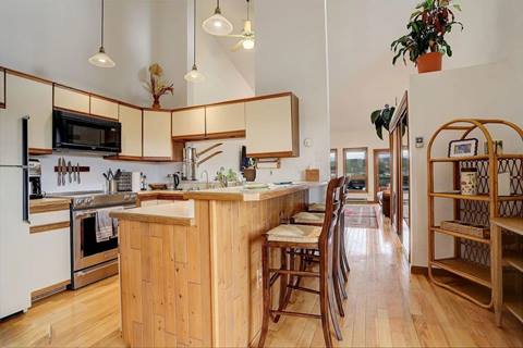 Modern kitchen with light wood cabinetry, stainless steel appliances, and a wooden breakfast bar with seating.