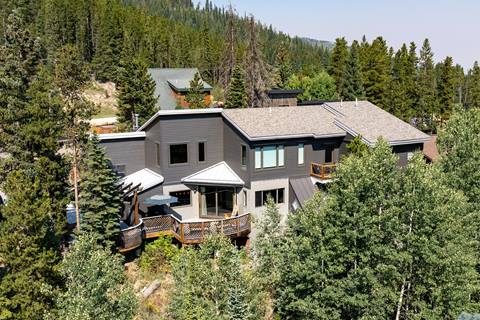 Exterior view of a large mountain home surrounded by evergreen trees, with a multi-level design and wooden deck.