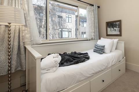 Bright bedroom with a daybed, white bedding, and large window framed by sheer curtains.