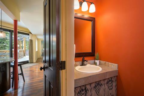 Half bathroom with bright orange walls, single vanity, mirror, and modern light fixture.