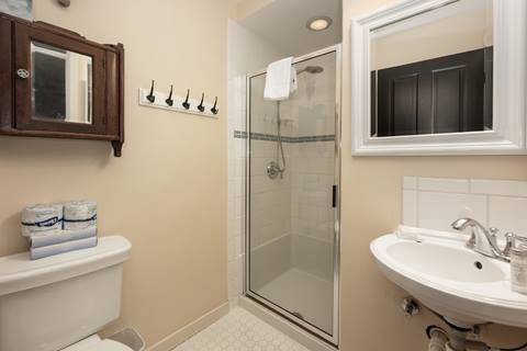 Bathroom with glass shower door, toilet, and small vanity with mirror.