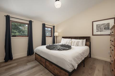 Bedroom with a queen bed, wood accents, and two windows with dark curtains.