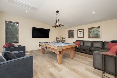 Game room with pool table, black leather sectional, and wall-mounted TV.