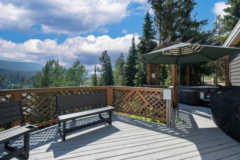 Spacious deck with benches, umbrella, hot tub, and grill overlooking mountain and forest views.