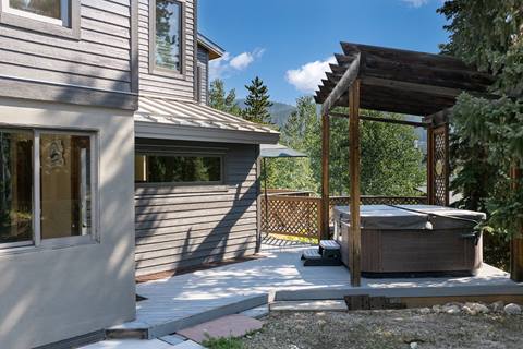 Hot tub beneath a wooden pergola, adjacent to the house with a private deck area.