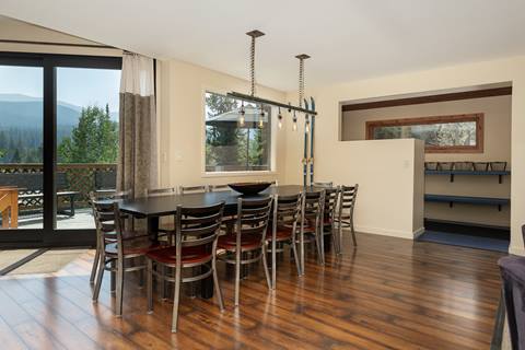 Dining room with a long black table and seating for twelve, opening to a deck with mountain views.