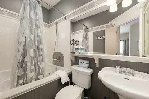 Bathroom with pedestal sink, toilet, and bathtub with floral shower curtain and decorative trim.