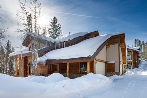 Snow-covered mountain townhome exterior with wood and stone accents, garage, and icicles hanging from the roof.