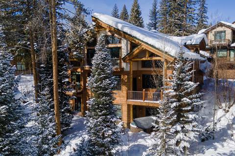 Back view of a multi-level mountain home surrounded by pine trees, balconies, and snow-covered landscape.