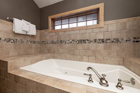 Close-up of soaking tub surrounded by tiled walls with decorative stone inlay.