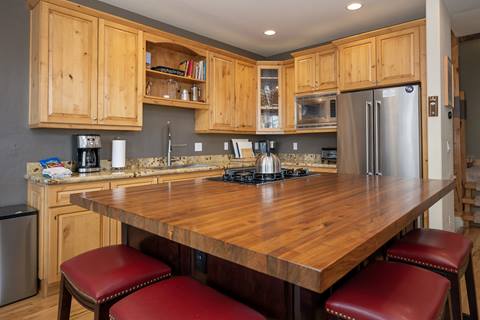 Kitchen with natural wood cabinets, stainless steel appliances, and a large wooden island with red cushioned stools.
