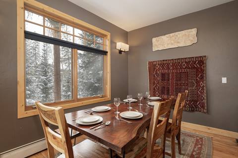 Dining area with wooden table set for six, large window with forest view, and decorative tapestry on the wall.