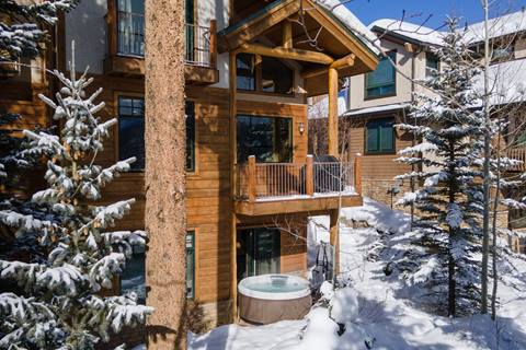 Private outdoor hot tub beneath a wooden deck, nestled in snowy pine trees behind the home.