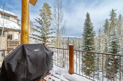 Snow-covered deck with a Weber grill and scenic forest views.