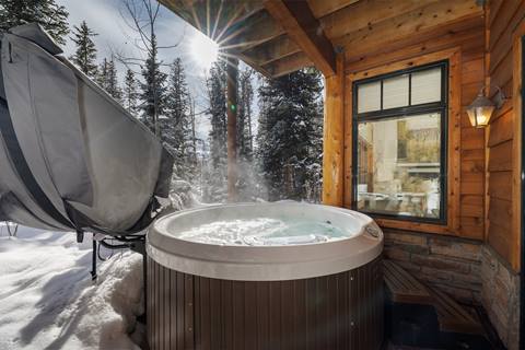 Outdoor hot tub steaming in a snowy wooded setting beside the cabin.