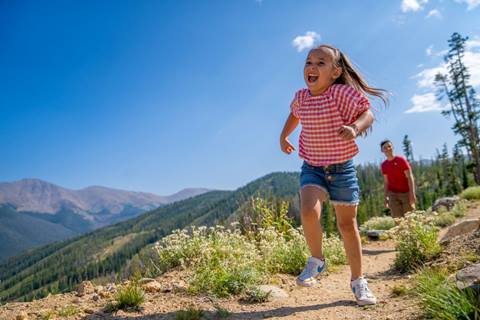 Girl running on mountainside with sibling at Winter Park Resort in Colorado