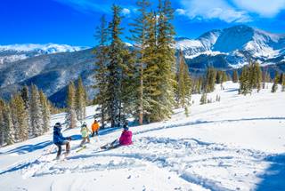 Group of people on a ski run with trees and mountains