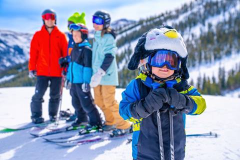 Kid smiling at camera with family in the background at Winter Park ski resort Colorado