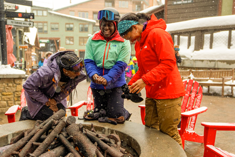 3 women laughing around a fire pit at Winter Park Resort