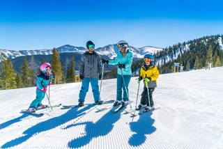 Family of 4 soaks up the sun on the slopes of winter park.