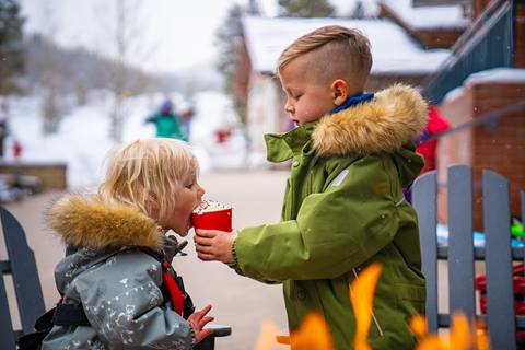 Two kids in the village at winter park drinking hot cocoa