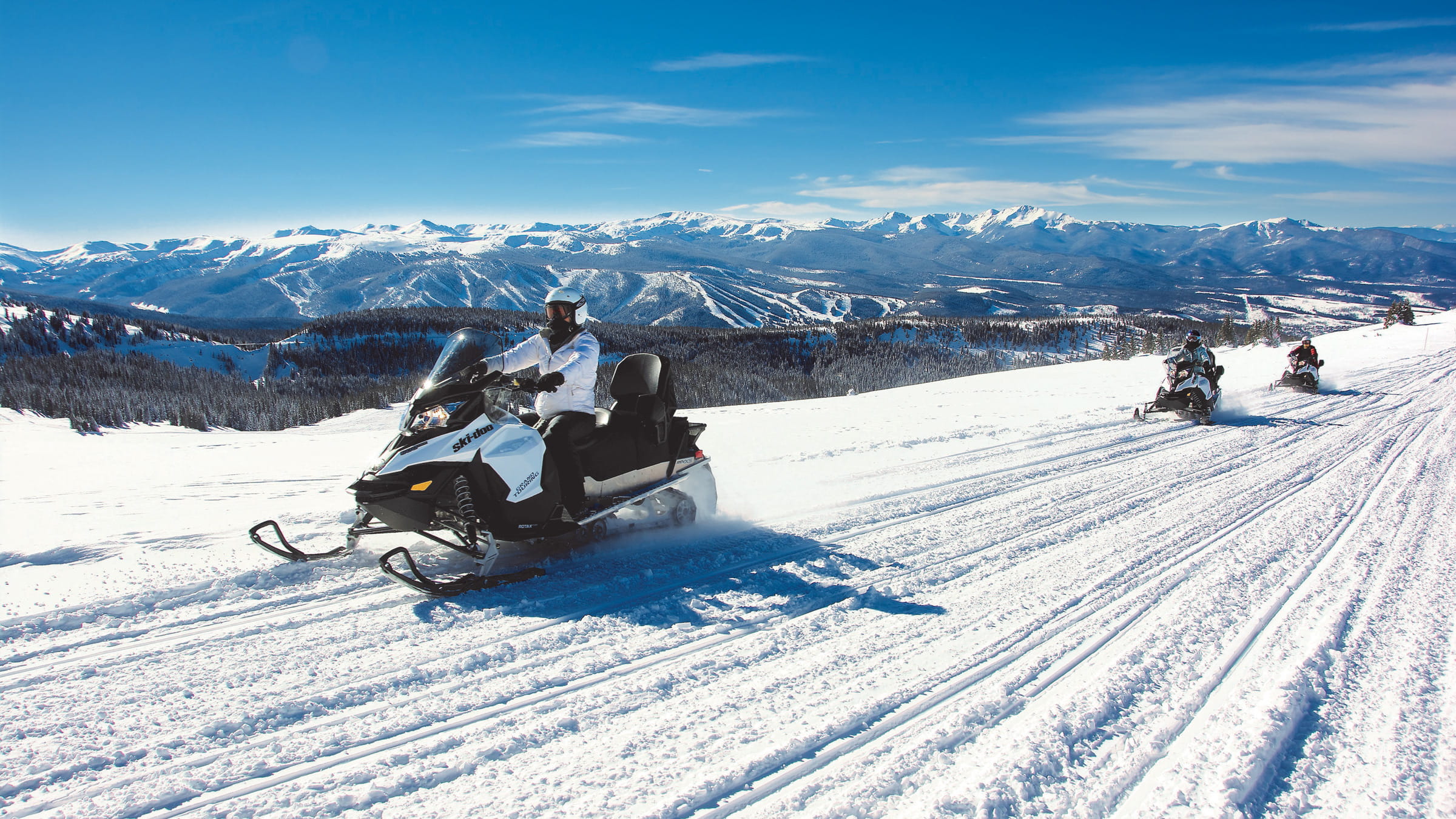 Group snowmobiles across the Continental Divide with a view of Winter Park Resort